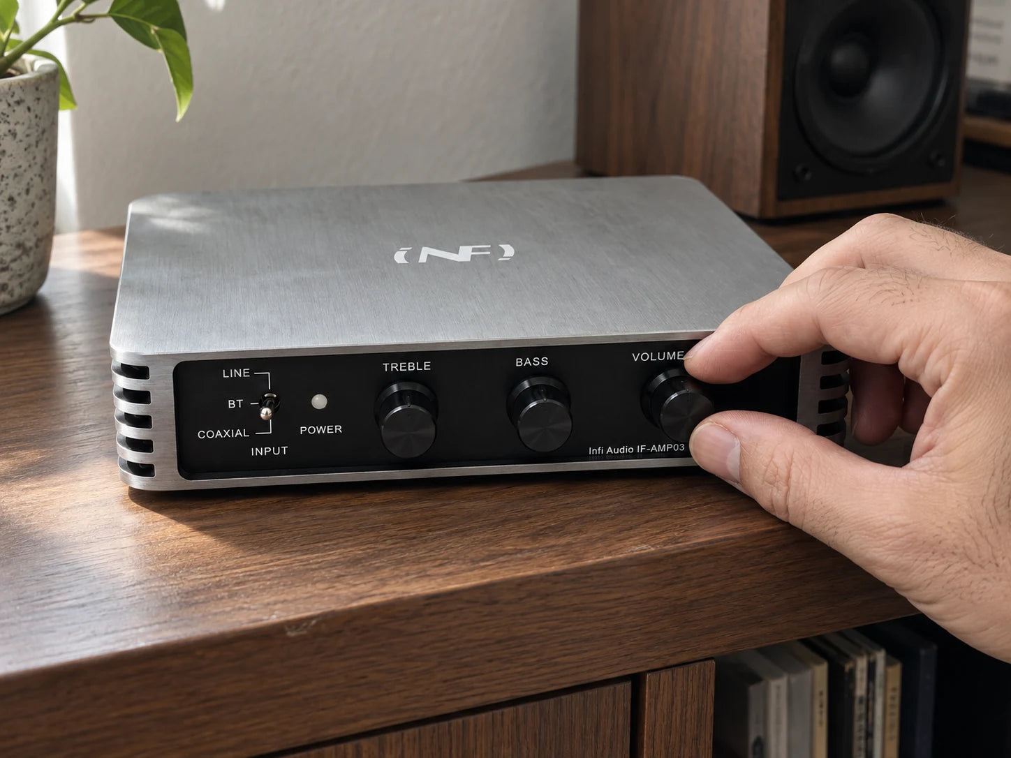 A hand adjusting the volume knob on the Infi Audio IF-AMP03 amplifier